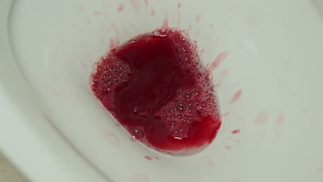 blood from menstruation cup emptied in toilet and flushed down, close up