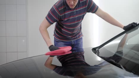 trabajador rojo está procesando la superficie del coche con una máquina de pulido en un servicio de automóviles, cubriendo con una capa protectora