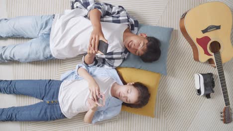 아시안 십대 커플이 집에서 바닥에 카에 누워 스마트폰을 연주하는  뷰. 전화 중독 커플