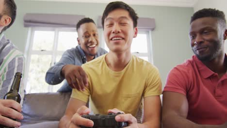 happy diverse male friends playing videogames and drinking beer in living room