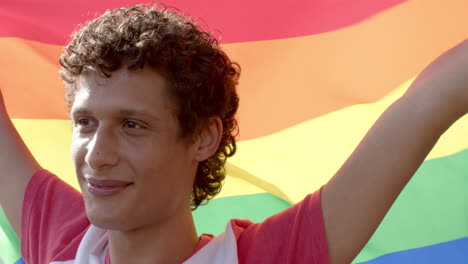 Happy-biracial-man-holding-rainbow-lgbt-flag-on-balcony-at-home,-slow-motion