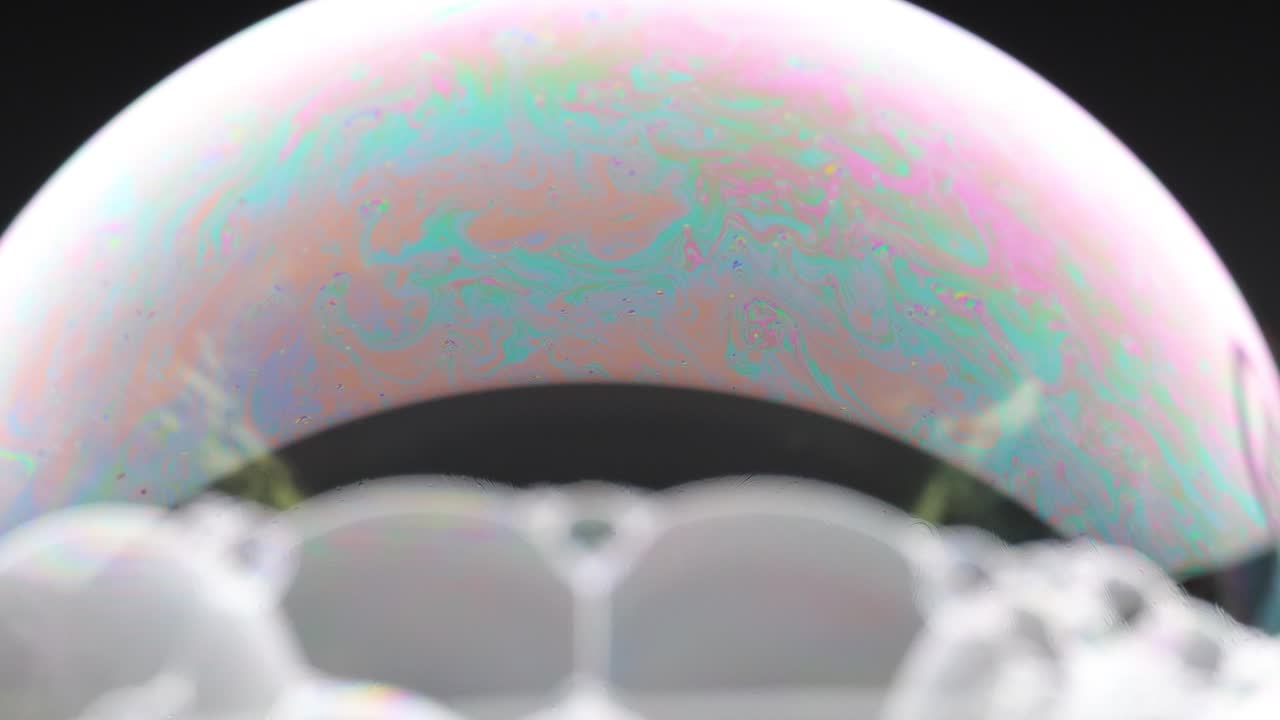 A soap bubble displays vibrant color patterns against a dark background, showcasing dynamic changes in light and texture