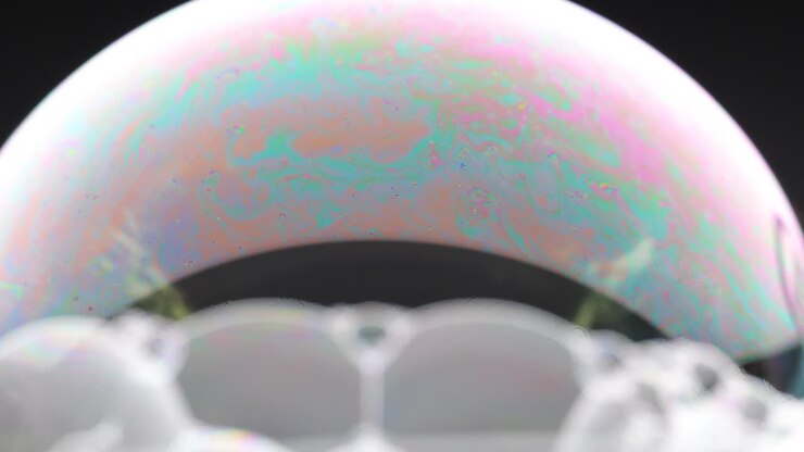 A soap bubble displays vibrant color patterns against a dark background, showcasing dynamic changes in light and texture