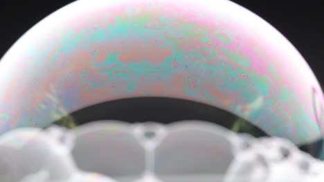 a soap bubble displays vibrant color patterns against a dark background, showcasing dynamic changes in light and texture