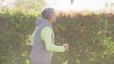 video of senior biracial man in sports clothes and headphones running in street