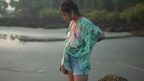 Beautiful-young-woman-walking-on-a-sandy-tropical-beach,-looking-down-on-ocean-water