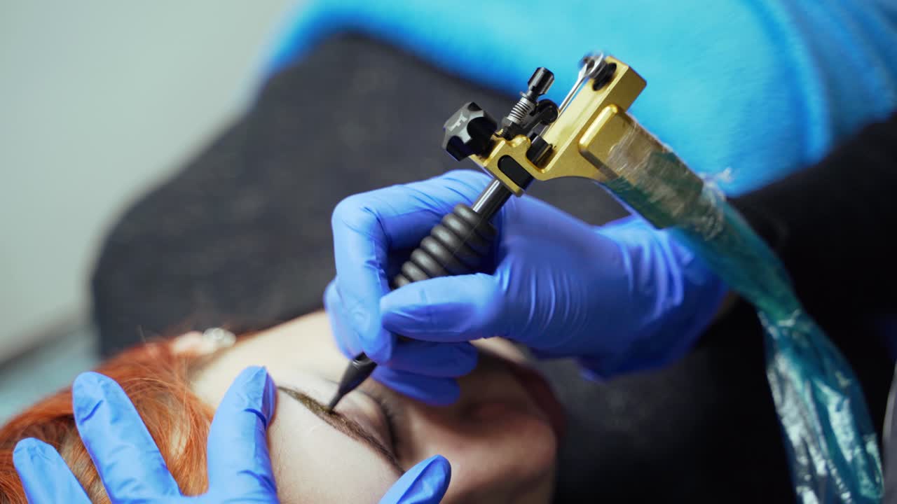 A beauty-master is doing eyebrow tattooing for the client using a special dye in the cosmetology. Blurred background. Close-up