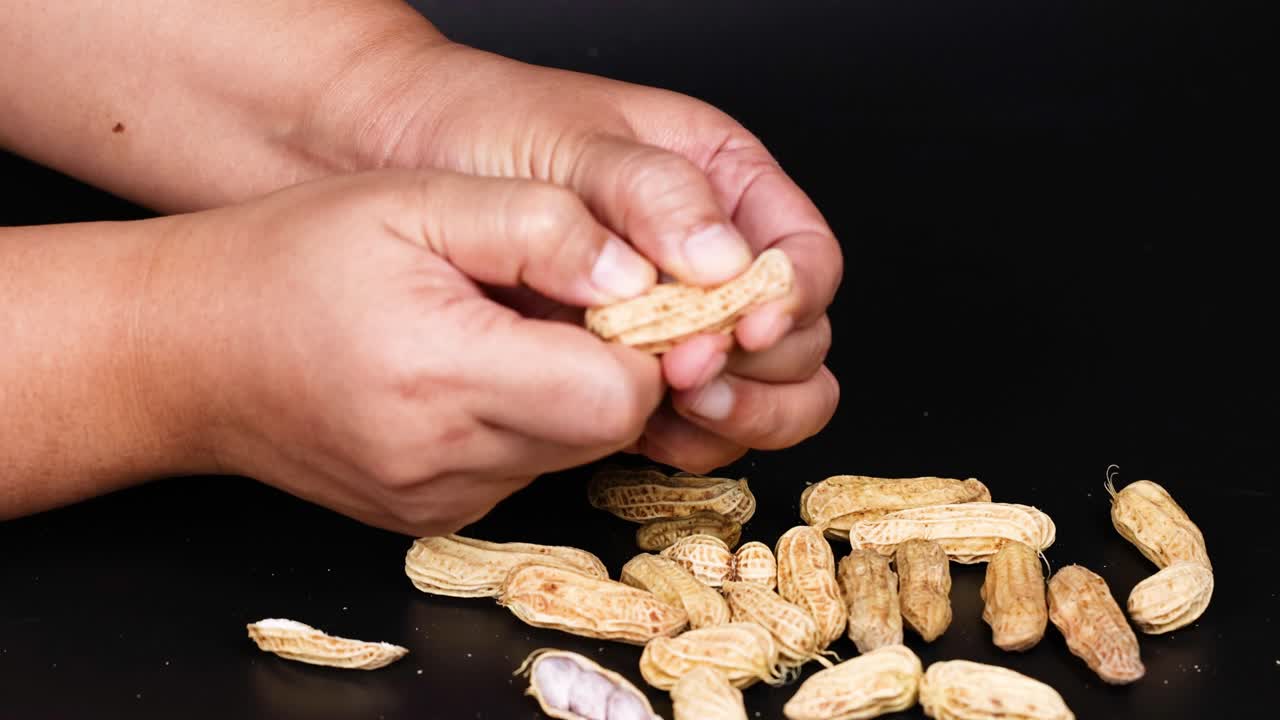 손 은 검은색 배경 에 땅콩 을 조심스럽게 벗기고 있다