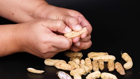 Hands carefully peeling peanuts on a black background