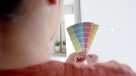 mujer biracial pensativa de tamaño grande mirando las tablas de colores de pintura en la sala de estar soleada, cámara lenta