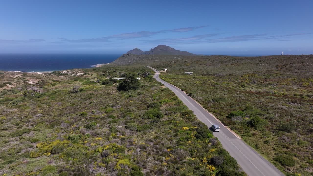 toma aérea de drones de una furgoneta conduciendo a lo largo de una hermosa carretera costera en el parque nacional de cape point en ciudad del cabo