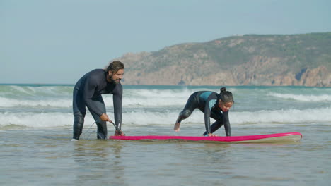 long shot of father teaching his daughter surfing