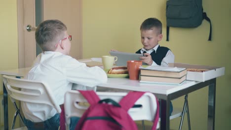 los escolares se sientan a la mesa con libros de texto, comida y bebidas