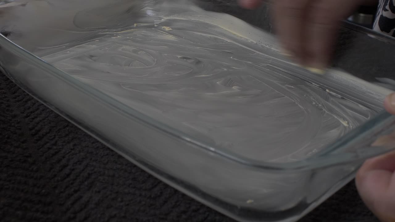 Mulher adulta untando o interior de travessa Pyrex com manteiga