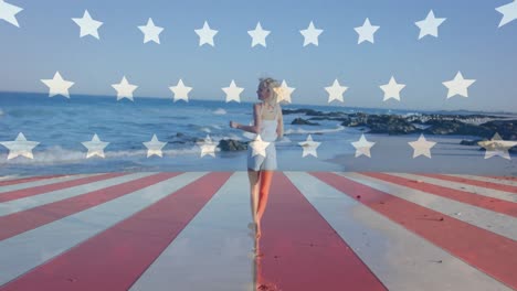 animation of flag over america over happy caucasian woman walking towards sea at beach