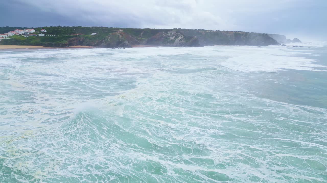 Waves crash near cliffs under cloudy skies, dramatic coastline in Aljezur, Portugal