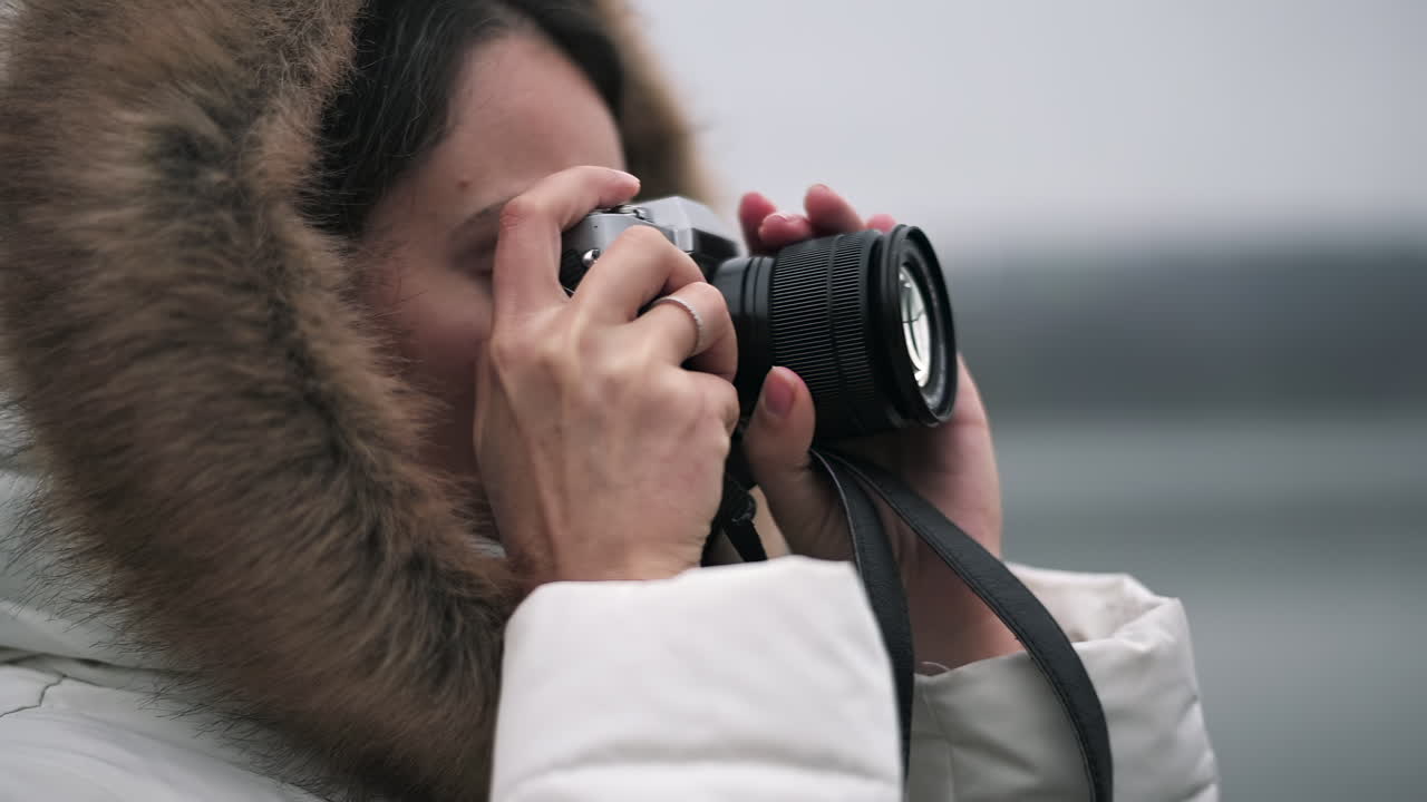 A person dressed warmly in a white coat with a fur-lined hood takes photos of the stunning snowy scenery. The cold environment enhances their focus on photography