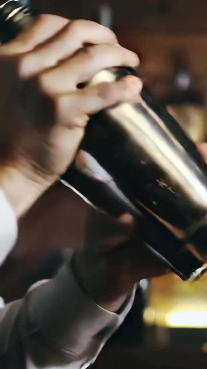 Video verticale: Barman che sigilla il coperchio e agita lo shaker al bar per preparare un drink, si vede un polsino bianco.