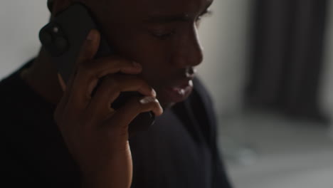 close up of angry young man standing in lounge at home having argument talking on mobile phone