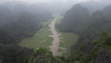 drone-shot-of-river-through-bright-green-rice-fields-and-dramatic-mountains-in-the-mountainous-region-of-Ninh-Ninh-in-Northern-Vietnam