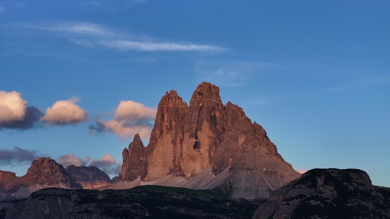 The famous Drei Zinnen mountains glow at sunset with soft clouds drifting above them