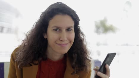 Girl-holding-cell-phone-and-smiling-at-camera