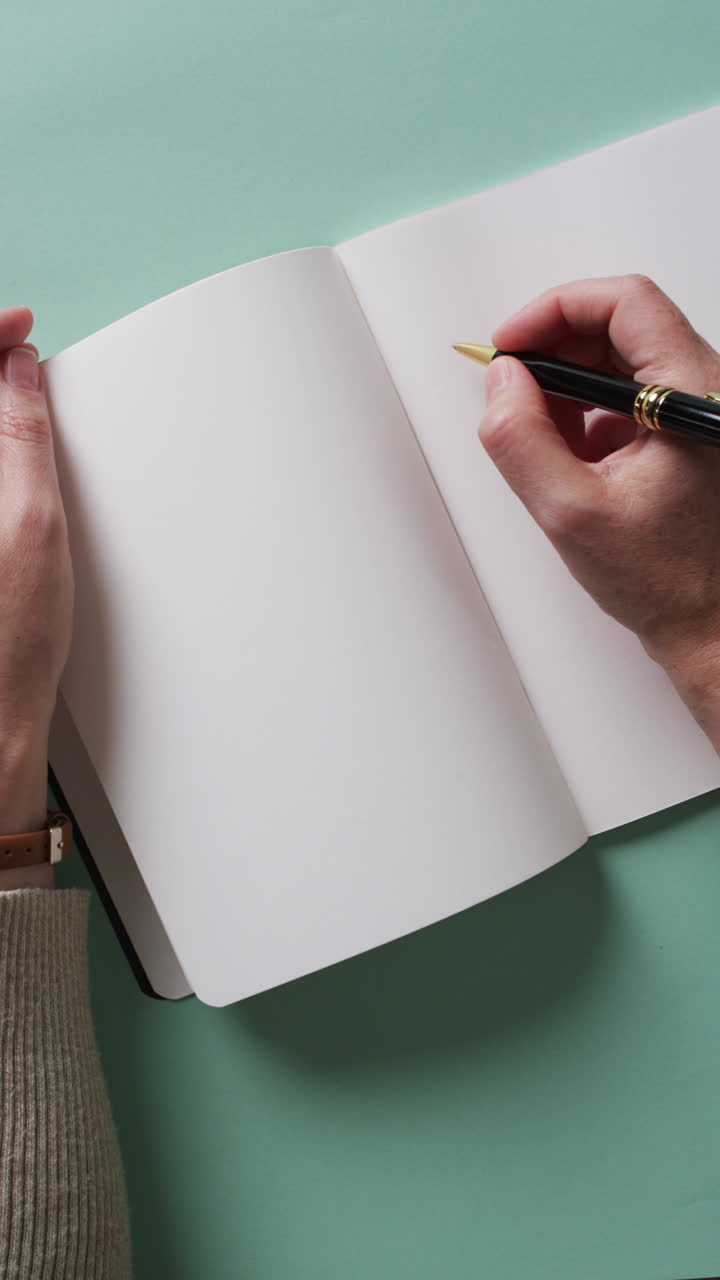 Vertical video of hand writing with pen on book with copy space on green background in slow motion