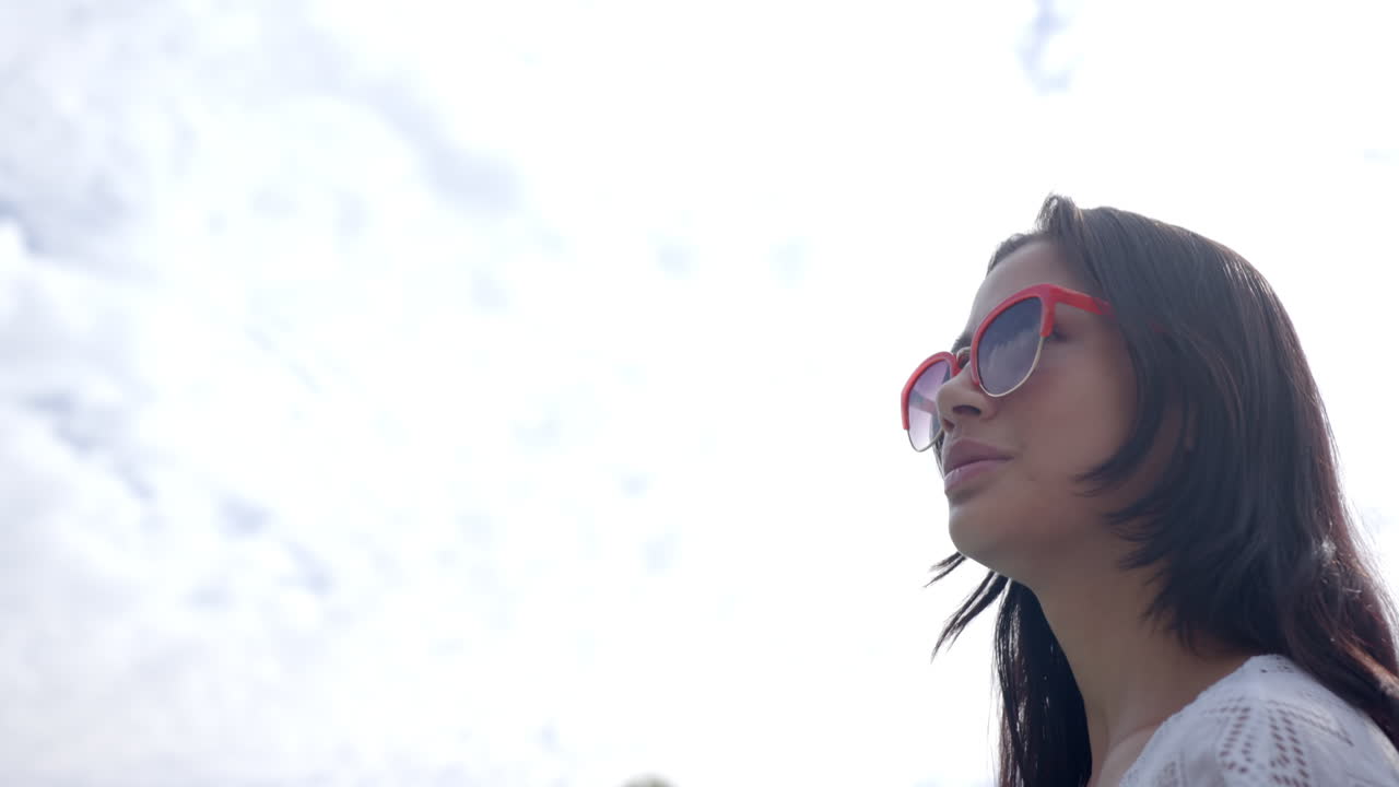 feliz adolescente biracial con gafas de sol sonriendo contra el cielo nublado soleado, copiar el espacio, cámara lenta
