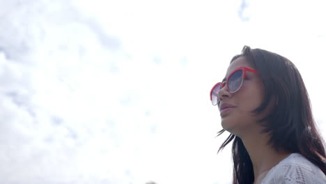 happy biracial teenage girl in sunglasses smiling against sunny cloudy sky, copy space, slow motion