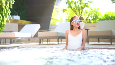 Attractive-Chinese-woman-sitting-in-spa-at-luxury-tropical-island-resort-as-water-swirls-in-foreground