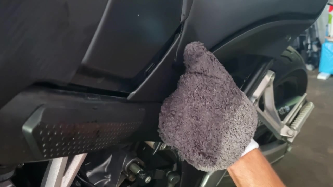 Close-up of a man’s hand carefully cleaning a motorcycle with a soft glove, focusing on detailed maintenance, vehicle care, polishing and motorbike hobby