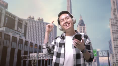 asian man freelancer with headphones using smartphone while standing in front of buildings working in a city