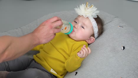 young one-year-old baby refuses to drink milk from father's hand while lying on a donut cushion