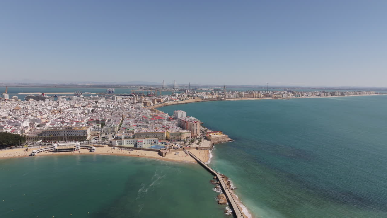 Ripresa aerea cinematografica con drone del paesaggio urbano di Cadice, in Spagna, Andalusia, Europa, in una luminosa giornata di sole, di fronte all'iconica e famosa spiaggia de La Caleta e al lungomare della città.