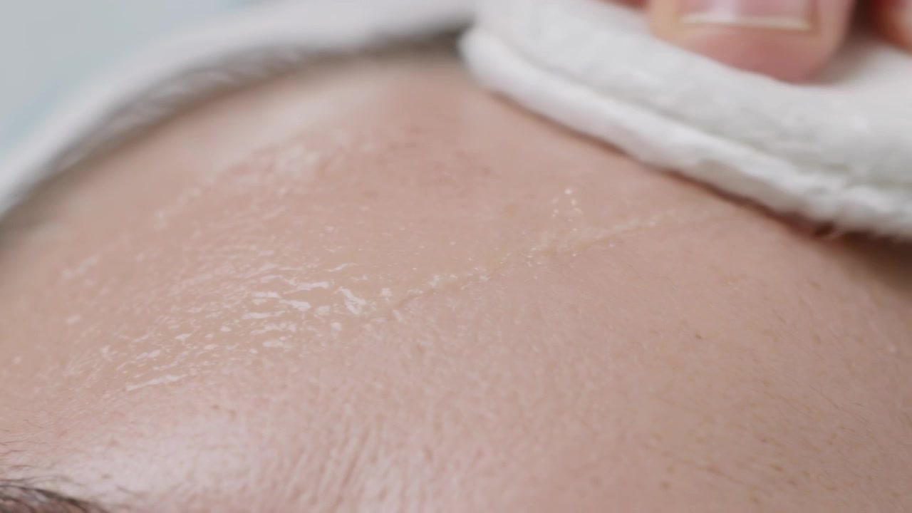 Donna che preme un dischetto di cotone sull'attaccatura dei capelli, asciugandosi la fronte al lavandino, mentre si pulisce con una fascia bianca.