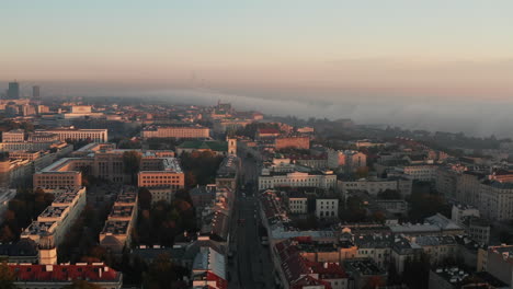 Forwards-fly-above-morning-town,-buildings-in-midtown.-Fog-around-river-in-background.-Warsaw,-Poland