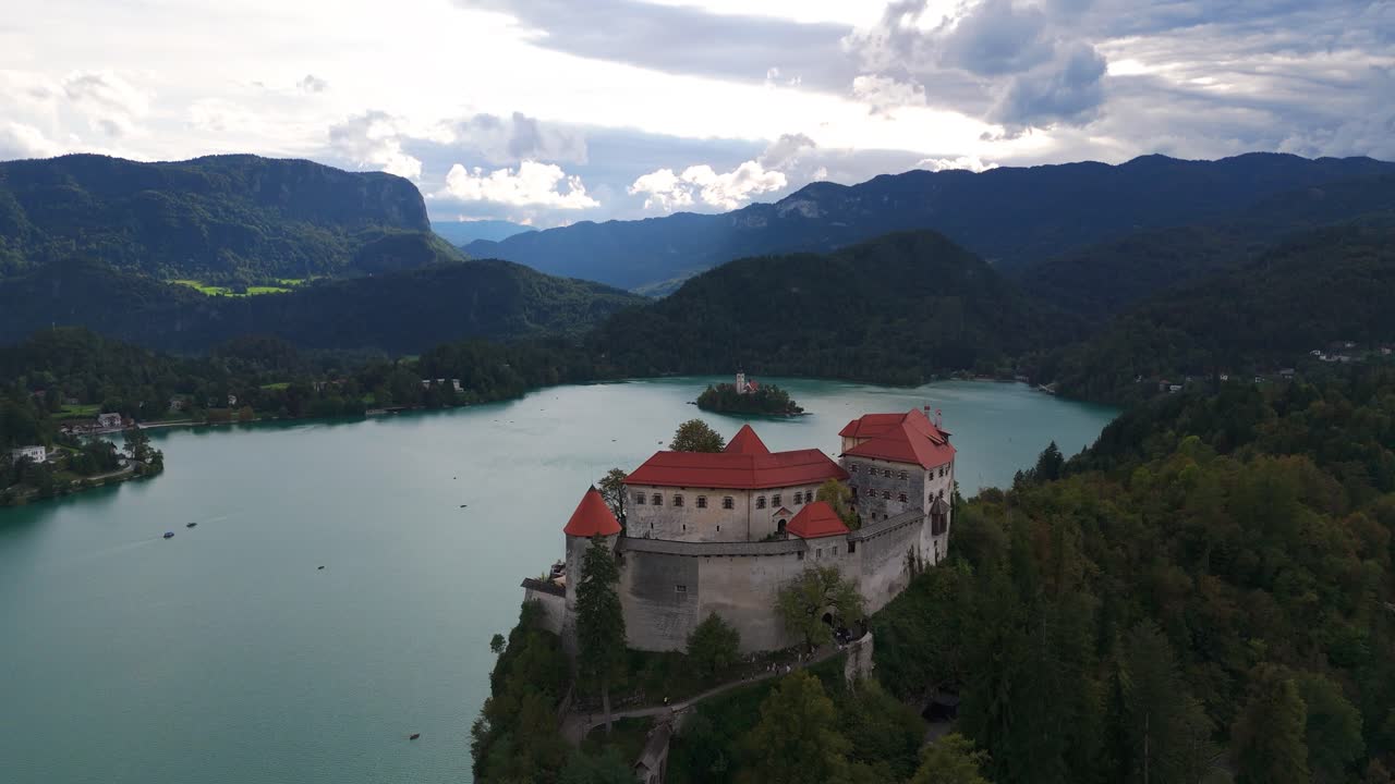 Carrellata aerea sul castello di Bled con vista sul lago di Bled, circondato da foreste e colline lontane, panoramica introduttiva