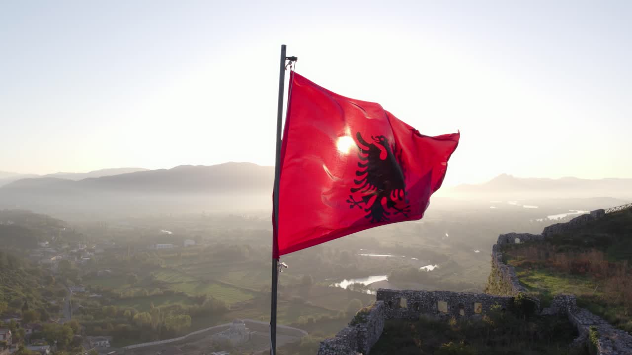 órbita alrededor de la bandera albanesa ondeando en el sol de la mañana en la parte superior del castillo, antena