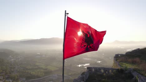 orbit around albanian flag waving in morning sun on top of castle, aerial