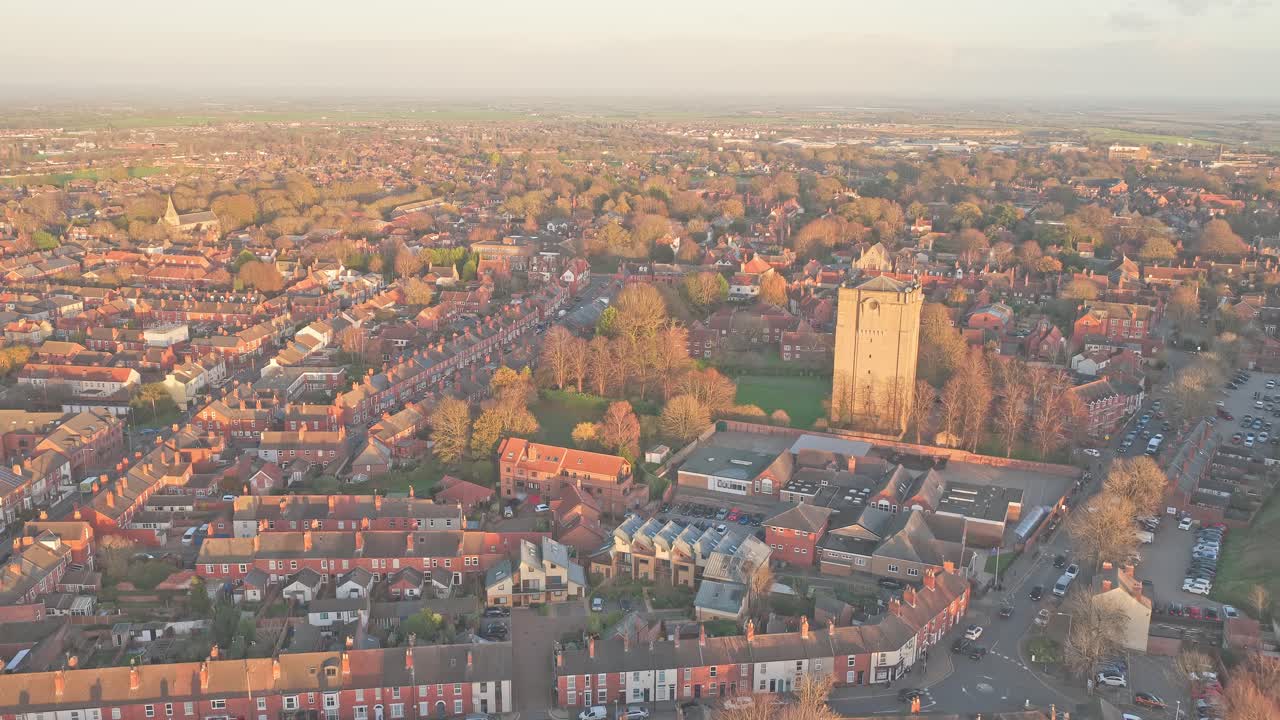 Lincoln's historic skyline and residential rooftops bathed in warm evening light, aerial view highlighting Westgate water tower, streets and peaceful urban landscape at golden hour