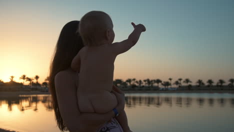 beautiful young mother holding little child on hands at sunset beach.