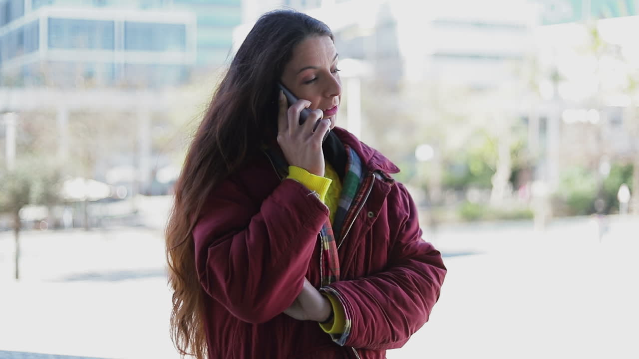 Cheerful mature woman in maroon jacket talking on phone outdoor