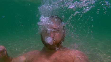 underwater view of bearded man breathing out air to create bubbles