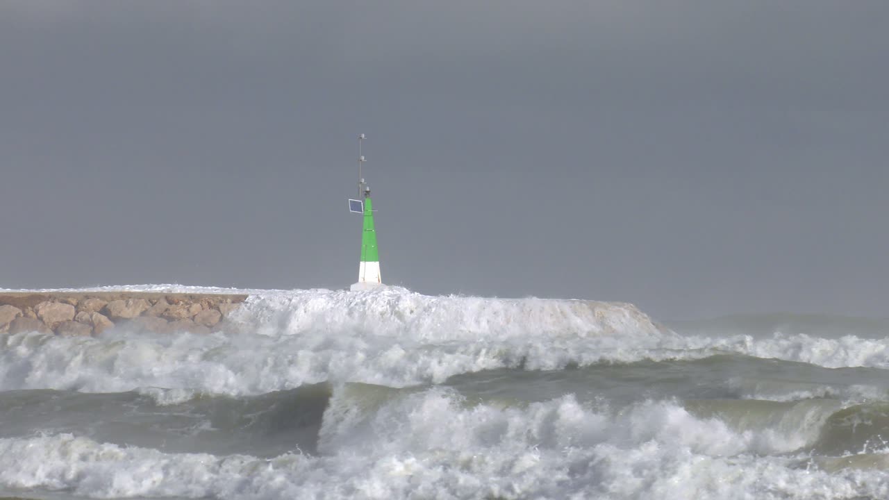 Powerful waves breaking over sea wall and harbor entrance light, slow motion