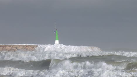 powerful waves breaking over sea wall and harbor entrance light, slow motion