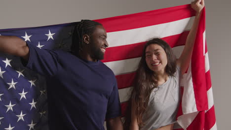 retrato de estudio de una pareja multicultural con una bandera estadounidense detrás de ellos celebrando el día de la independencia del 4 de julio