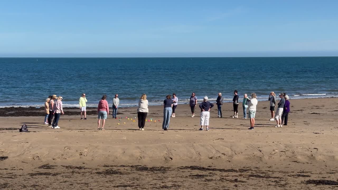 Women engage in a spirited match of beach bowls, enjoying the sun and sea breeze during the outdoor activity.
