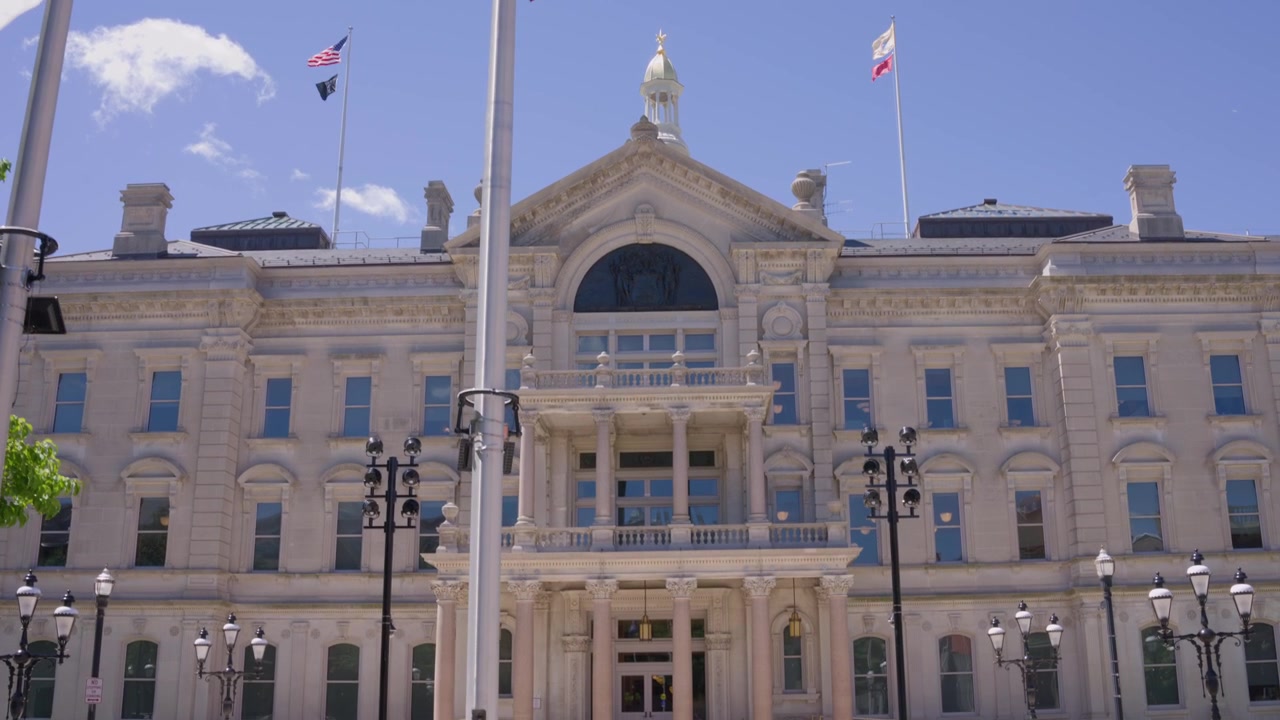 Ripresa cinematografica in tilt-down dalle bandiere americane che rivela il Campidoglio del New Jersey nel centro di Trenton, New Jersey, in una giornata di sole