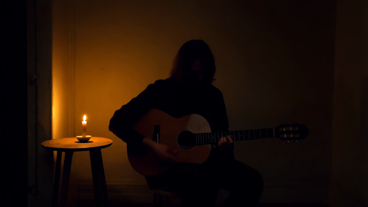 Silhouette of a Musician Playing Guitar in a Dark Room with Candlelight