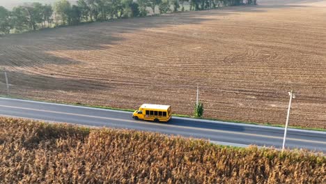 aerial tracking shot of short school bus driving on rural road in usa